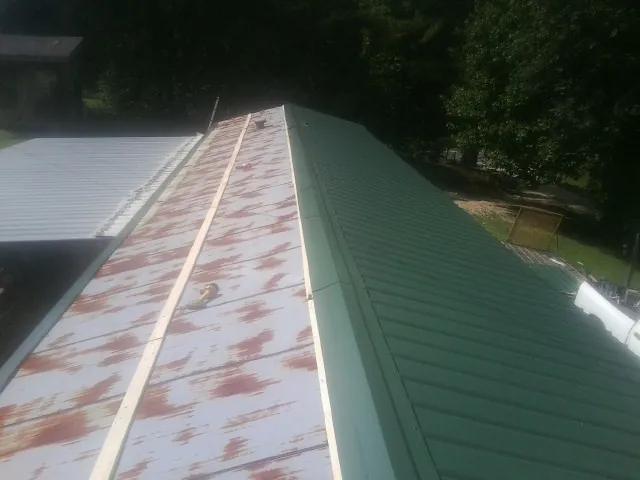 Old rusted panels beside newly installed green metal roofing — Wind Damage Roof Repair by Roofing Brothers in Swanton